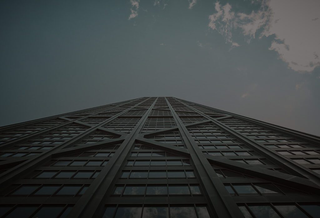A view looking up at a tall, dark skyscraper with a steel framework against a cloudy sky.