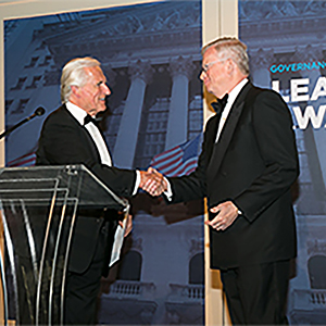 James Drury is shaking hands with another person standing behind a podium.