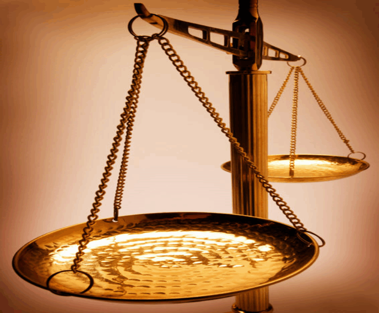 Close-up of a golden balance scale with one pan in the foreground and another in the background against a warm, softly lit backdrop.