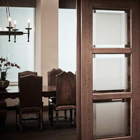A dining area with a wooden table and chairs is partially visible through a door with frosted glass panels. A chandelier hangs above the table.