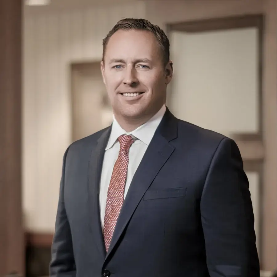 Casey Gober smiles at the camera. He is wearing a dark gray suite, red and gold spotted tie, and has short brown hair.