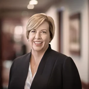 Lizabeth Hancock has short blonde hair and is smiling at the camera. She is wearing a black blazer over a white blouse.