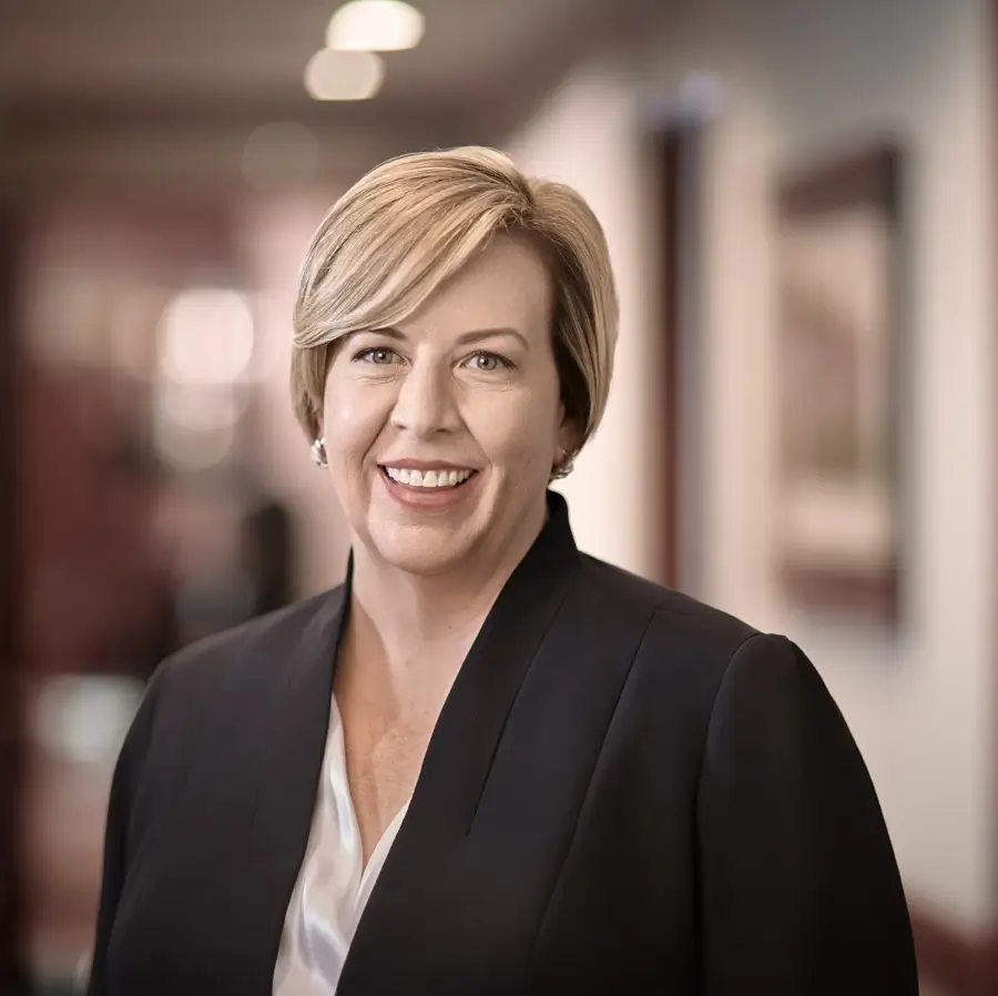 Lizabeth Hancock has short blonde hair and is smiling at the camera. She is wearing a black blazer over a white blouse.
