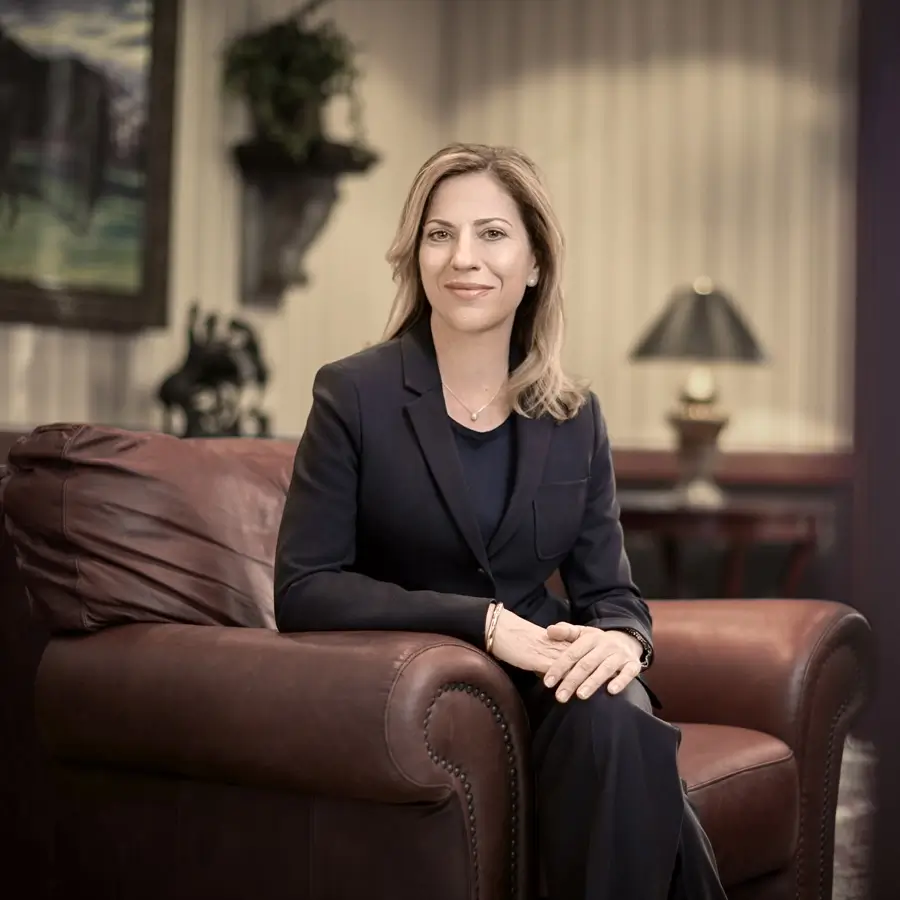 Nancy Konieczki is sitting in a large brown leather chair with her hands clasped on her crossed knees. She is wearing a black suite over a black top, with shoulder-length blonde hair.